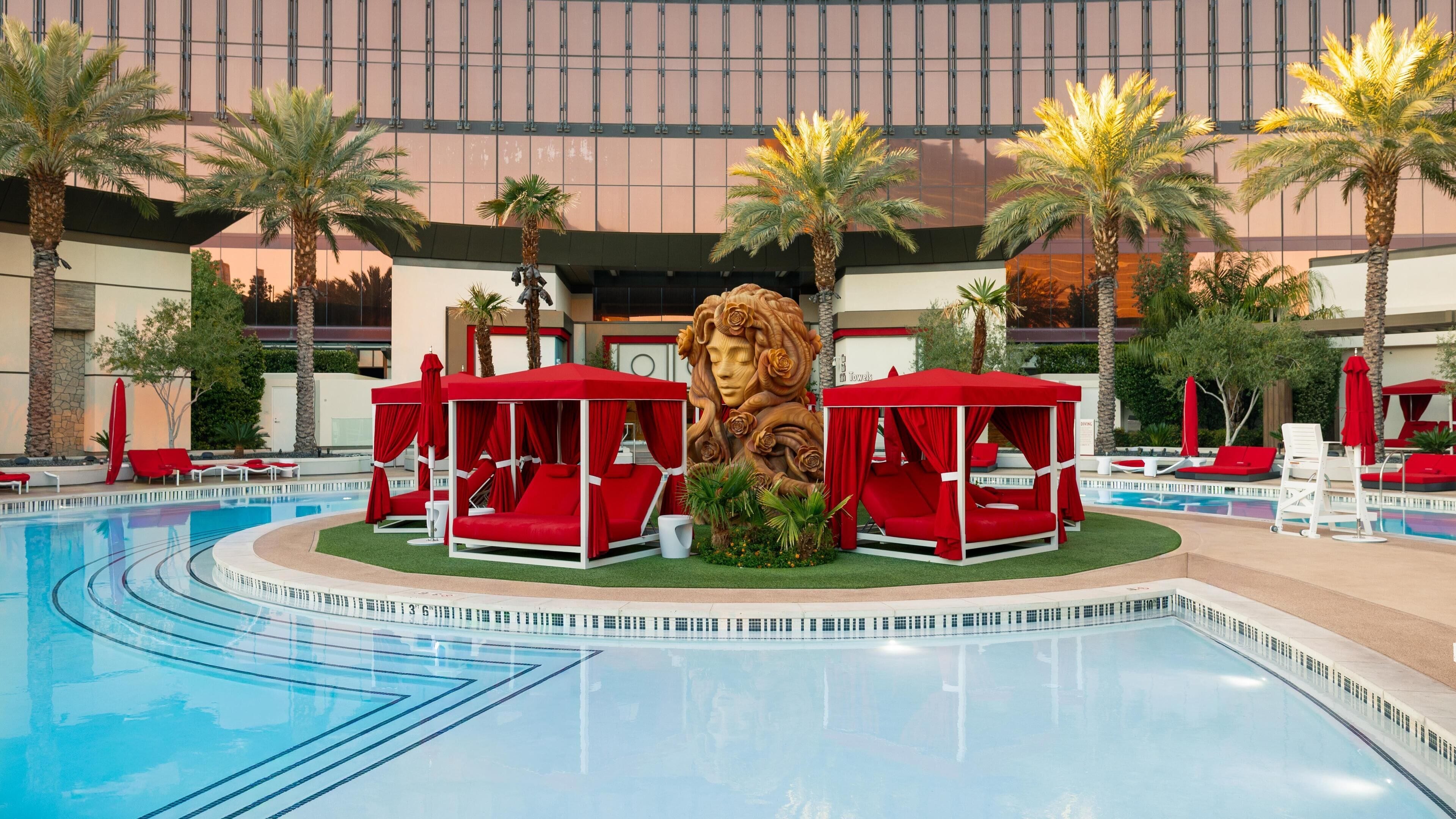 A swimming pool with red lounge chairs and a large decorative lion statue in the center.