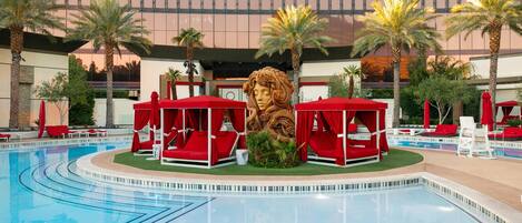 Una piscina con sillas de descanso rojas y una gran estatua decorativa de león en el centro.