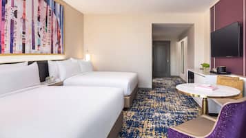 A hotel room with two beds, a round table, a purple chair, a TV, and a large abstract painting on the wall.