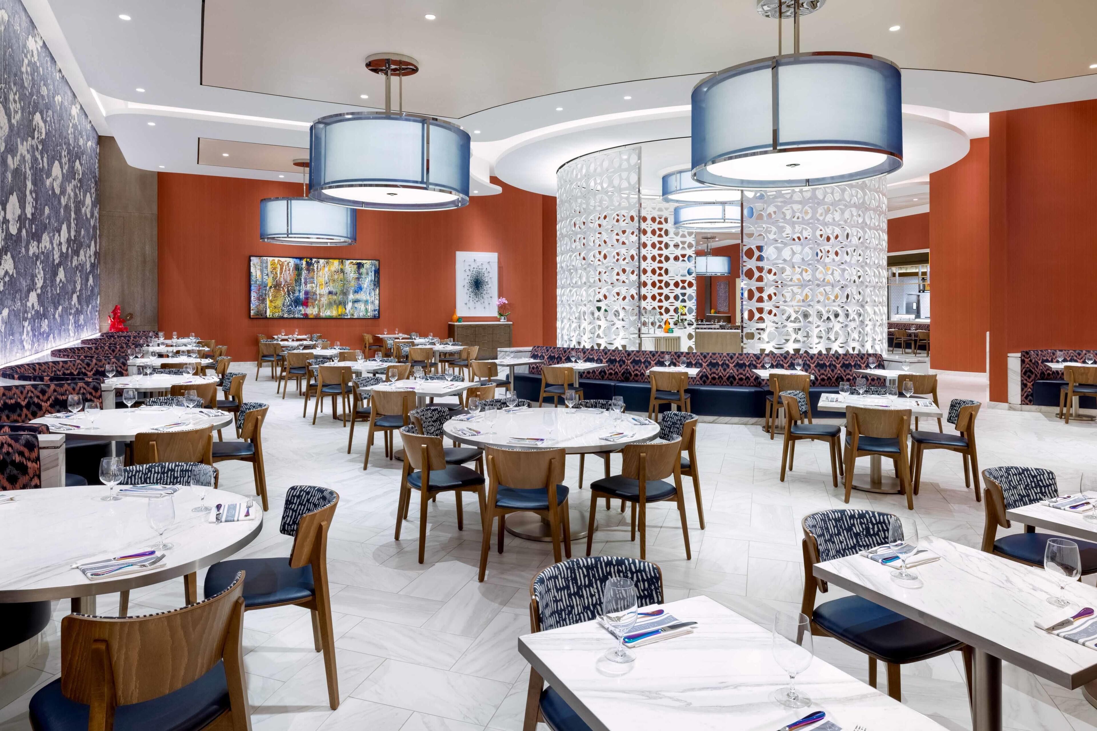 A modern dining area with round tables, blue upholstered chairs, and contemporary lighting fixtures.