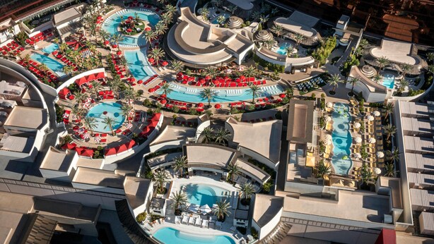 Vue aérienne d’un complexe hôtelier doté de plusieurs piscines, de chaises longues et de palmiers.