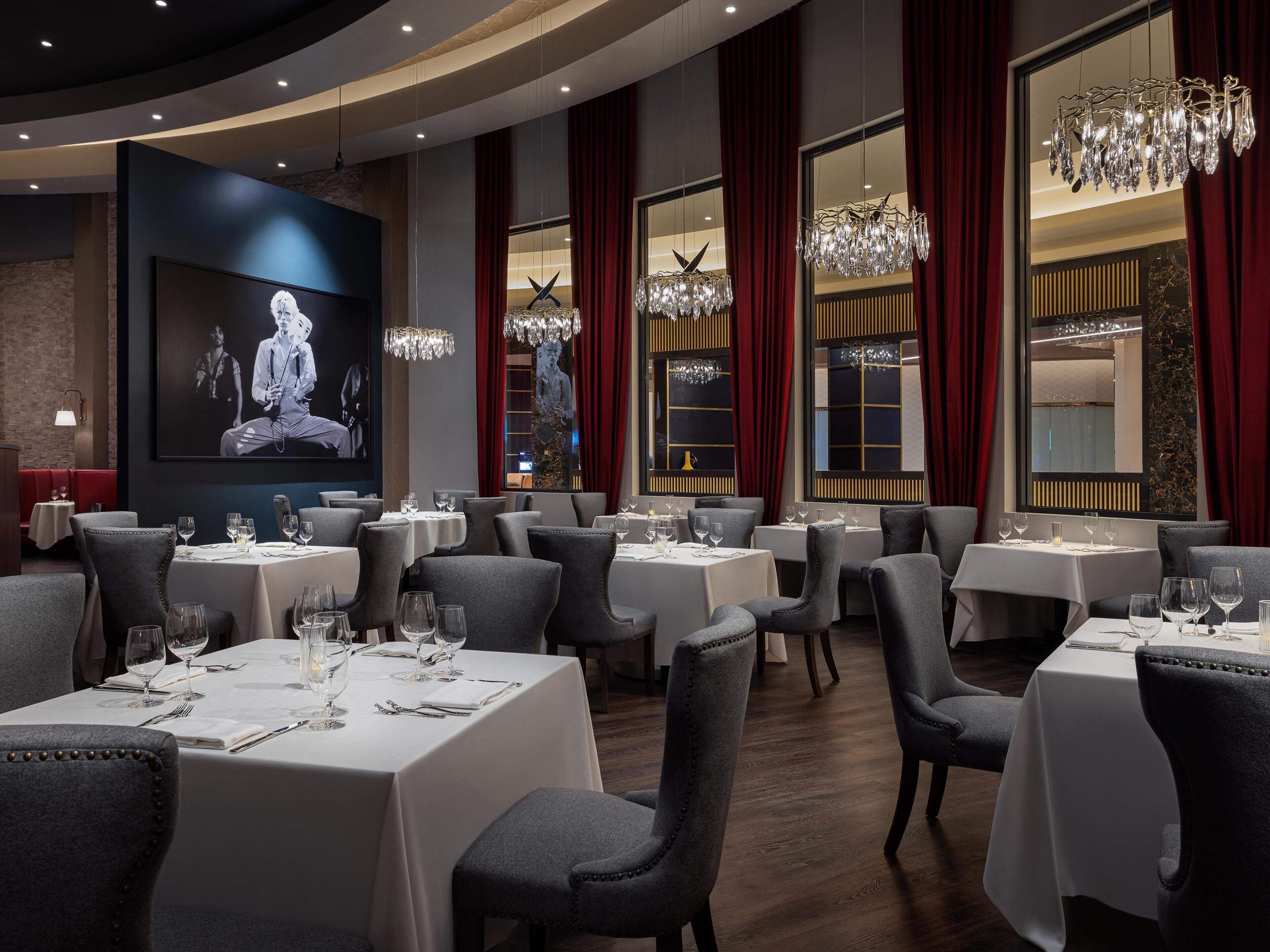 A restaurant with multiple tables, elegant chandeliers, and a large screen displaying a movie.