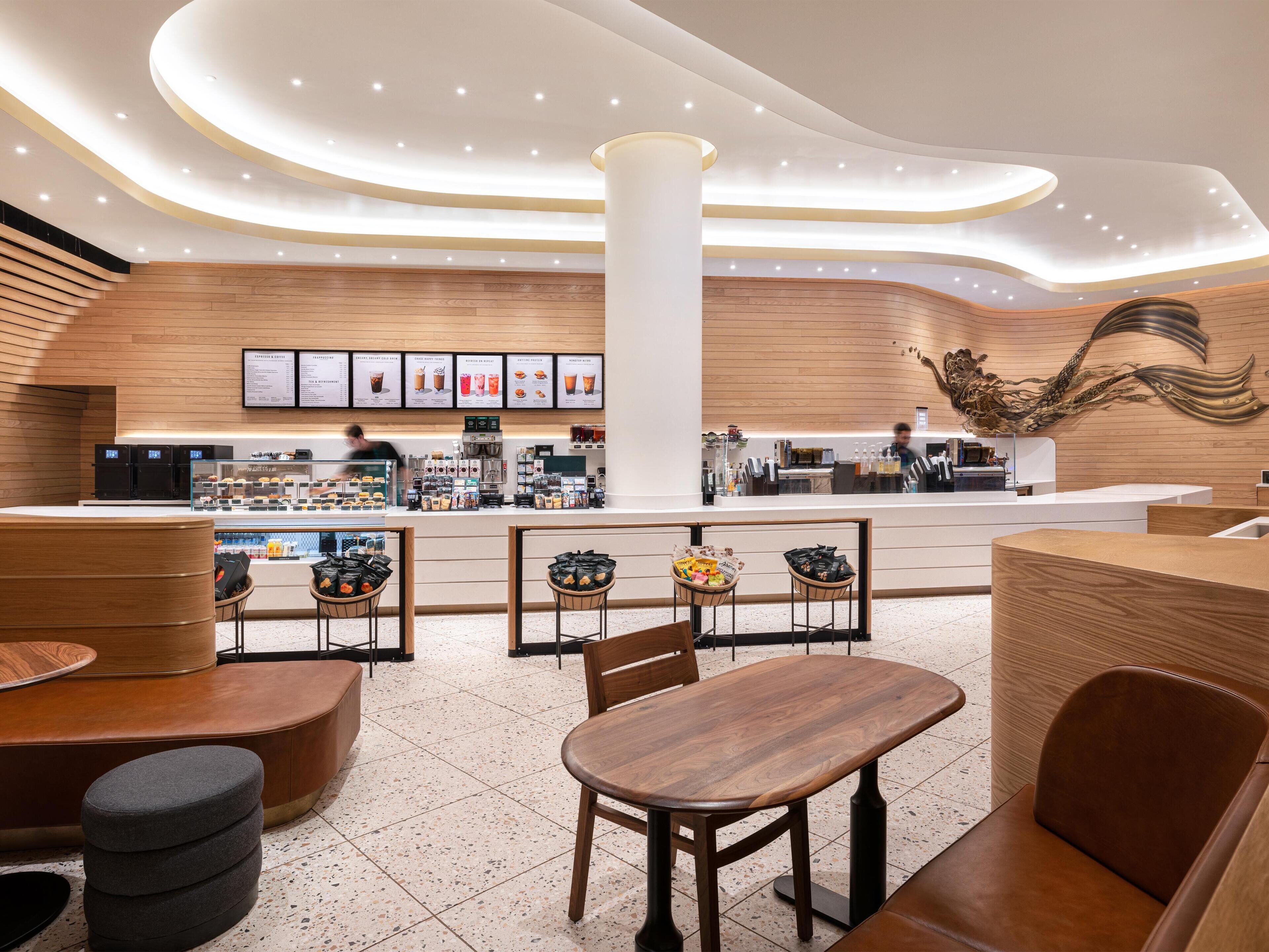 A modern cafe with a central counter, seating area, and a decorative wall mural.