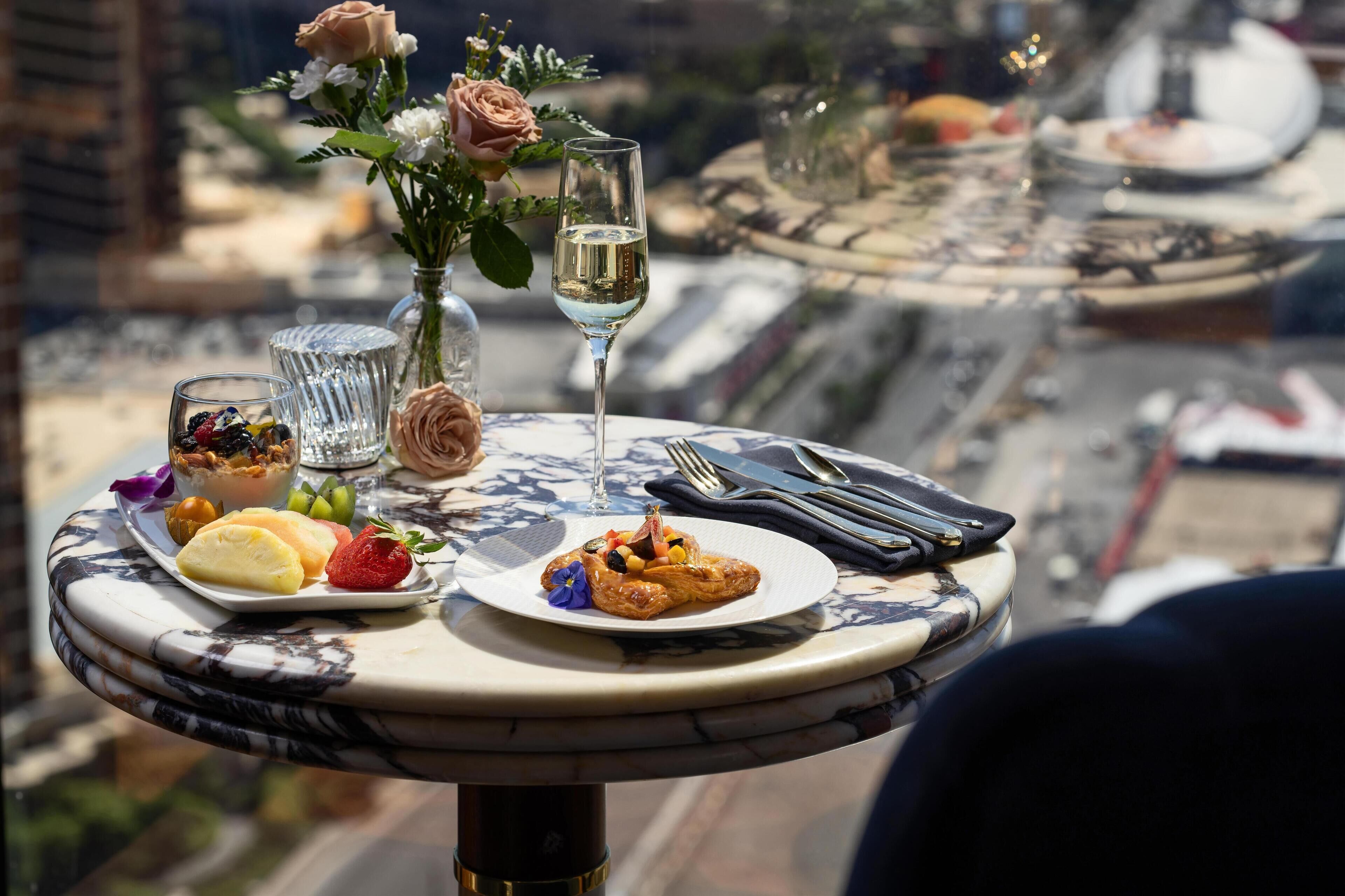 A table with a glass of white wine, a plate of food, and a vase of flowers.