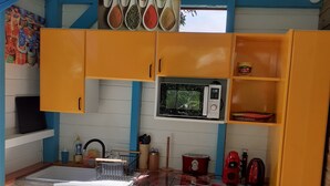 A kitchen with yellow cabinets, a microwave, a sink, and various kitchen utensils. - "LE TI-COLIBRI" CHARMING BUNGALOW at the foot of "La Soufrière" volcano (Saint-Claude)