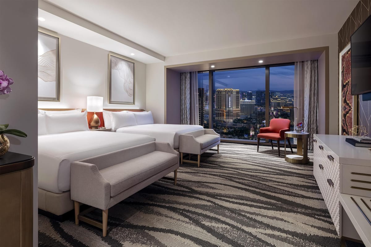A hotel room with two beds, a desk, a chair, and a large window offering a city view.