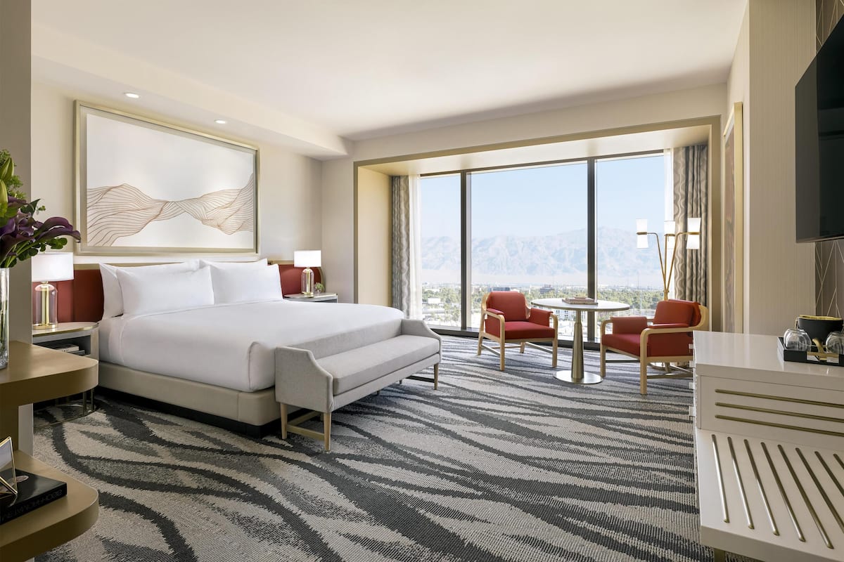 A hotel room with a large bed, a desk, a chair, and a view of the mountains.