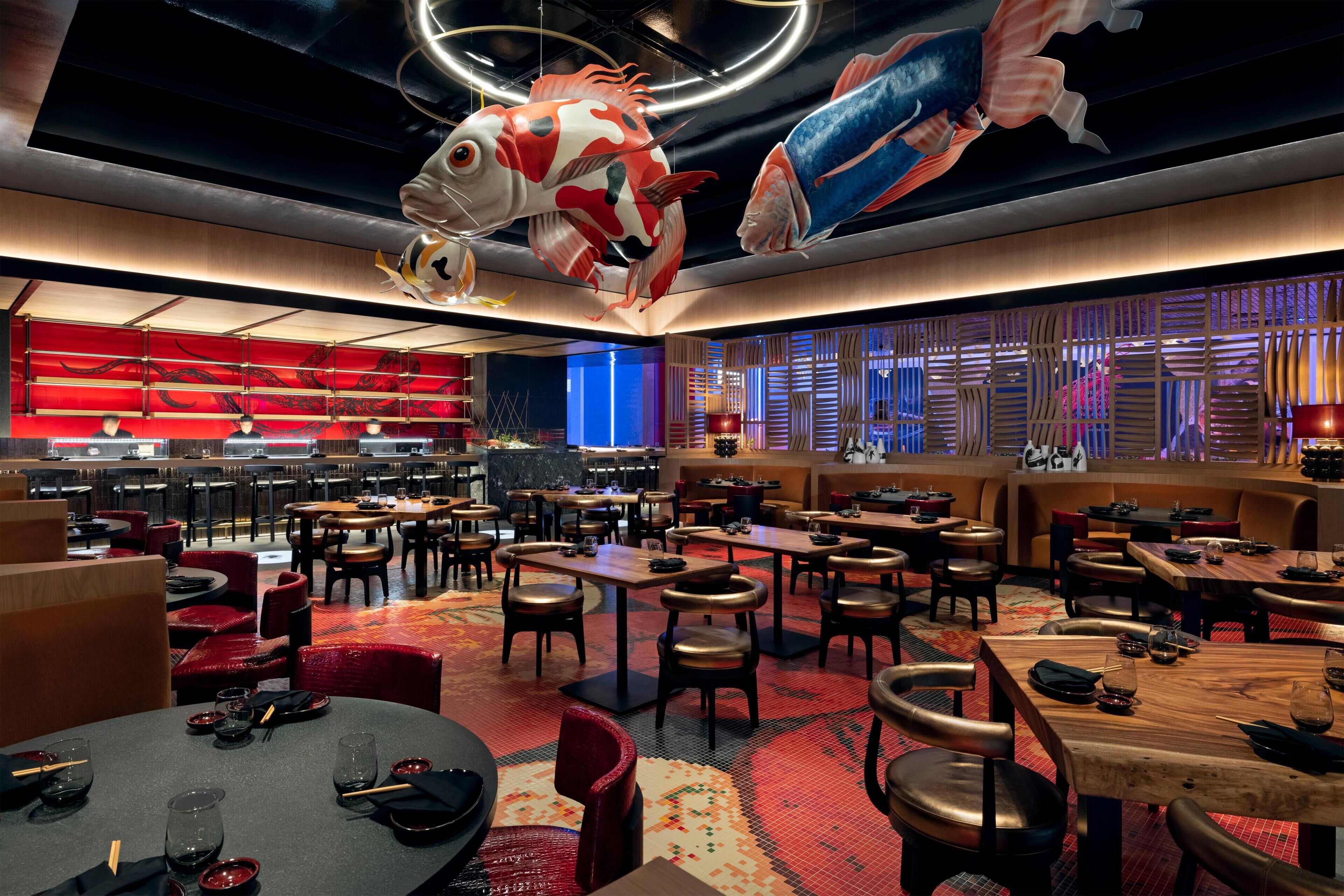 Un restaurante espacioso con varias zonas de comedor, decoración en rojo y azul, y grandes esculturas de peces en el techo.