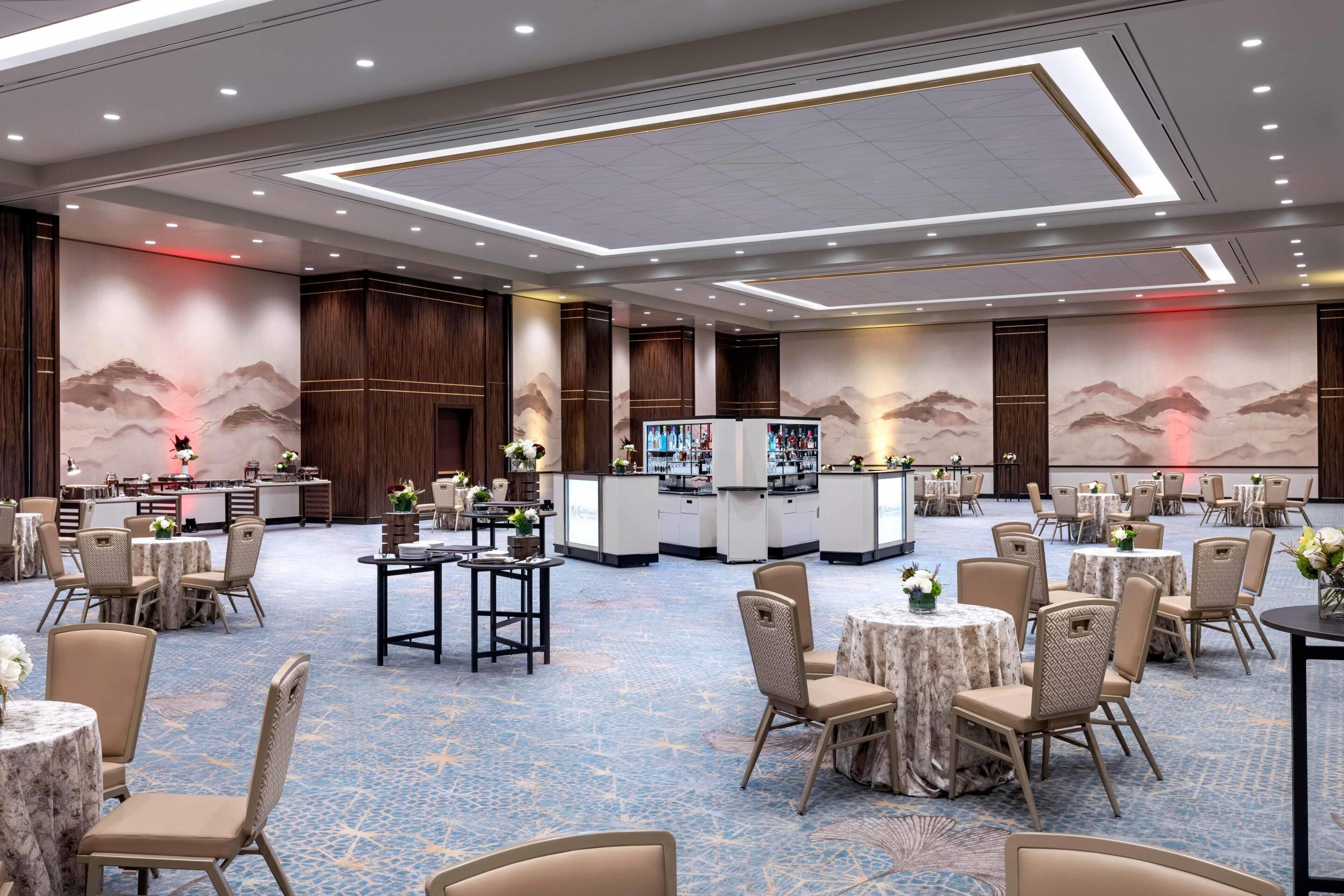 A spacious banquet hall with round tables and chairs, a bar area, and decorative wall murals.