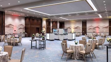A spacious banquet hall with round tables and chairs, a bar area, and decorative wall murals.