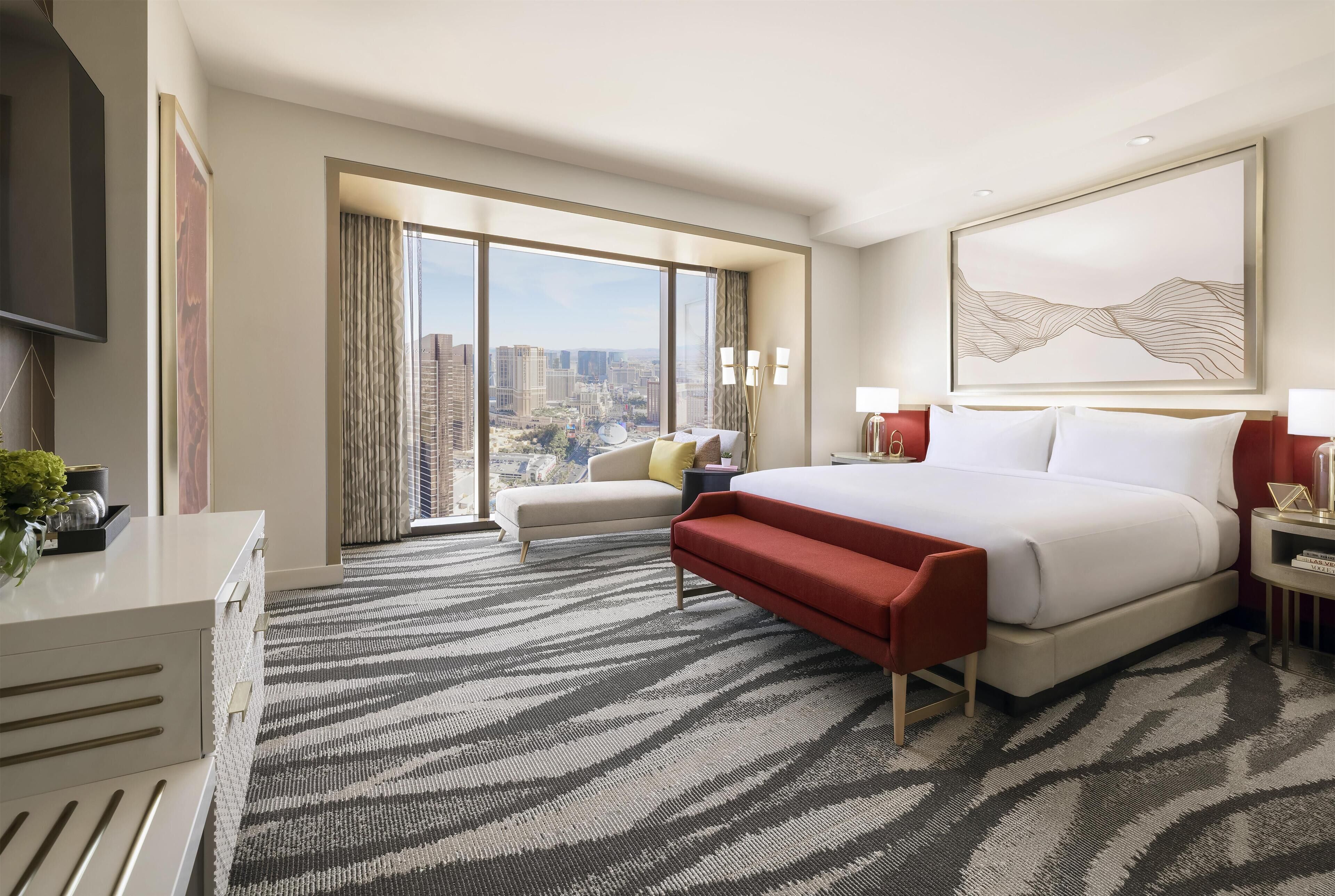 A hotel room with a large bed, a sofa, a desk, and a view of the city.