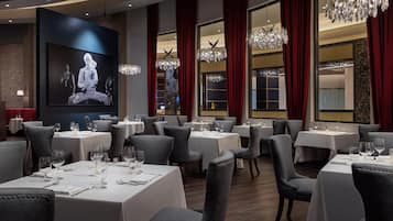 A restaurant with multiple tables, elegant chandeliers, and a large screen displaying a movie.