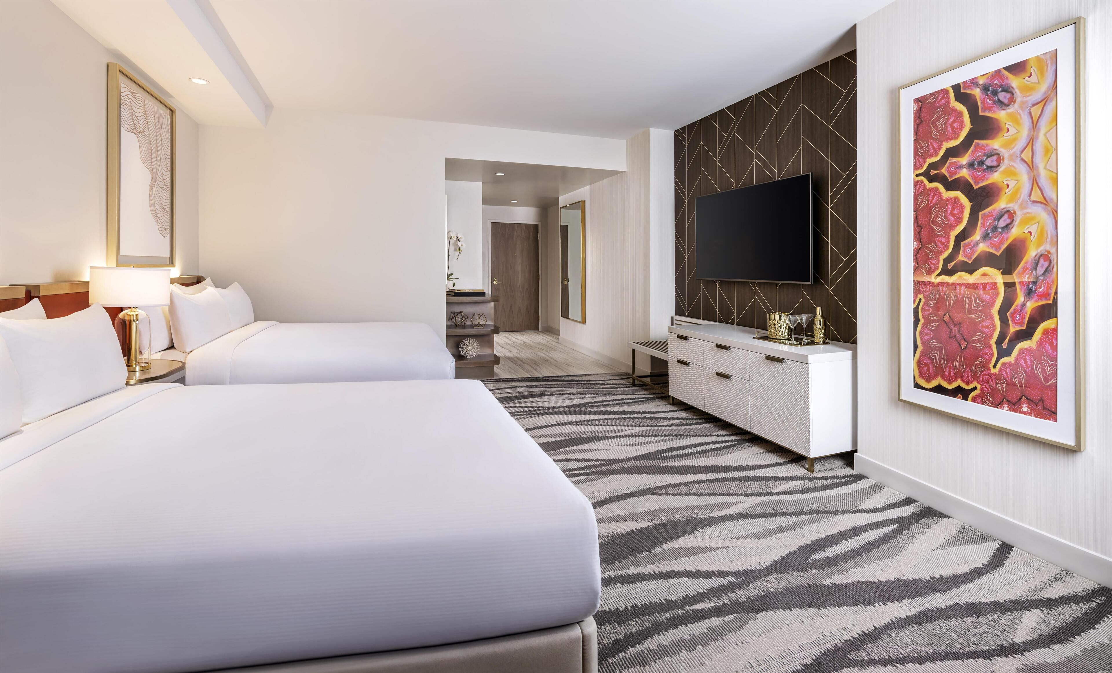 A hotel room with two beds, a large TV, a modern art piece, and a minibar.