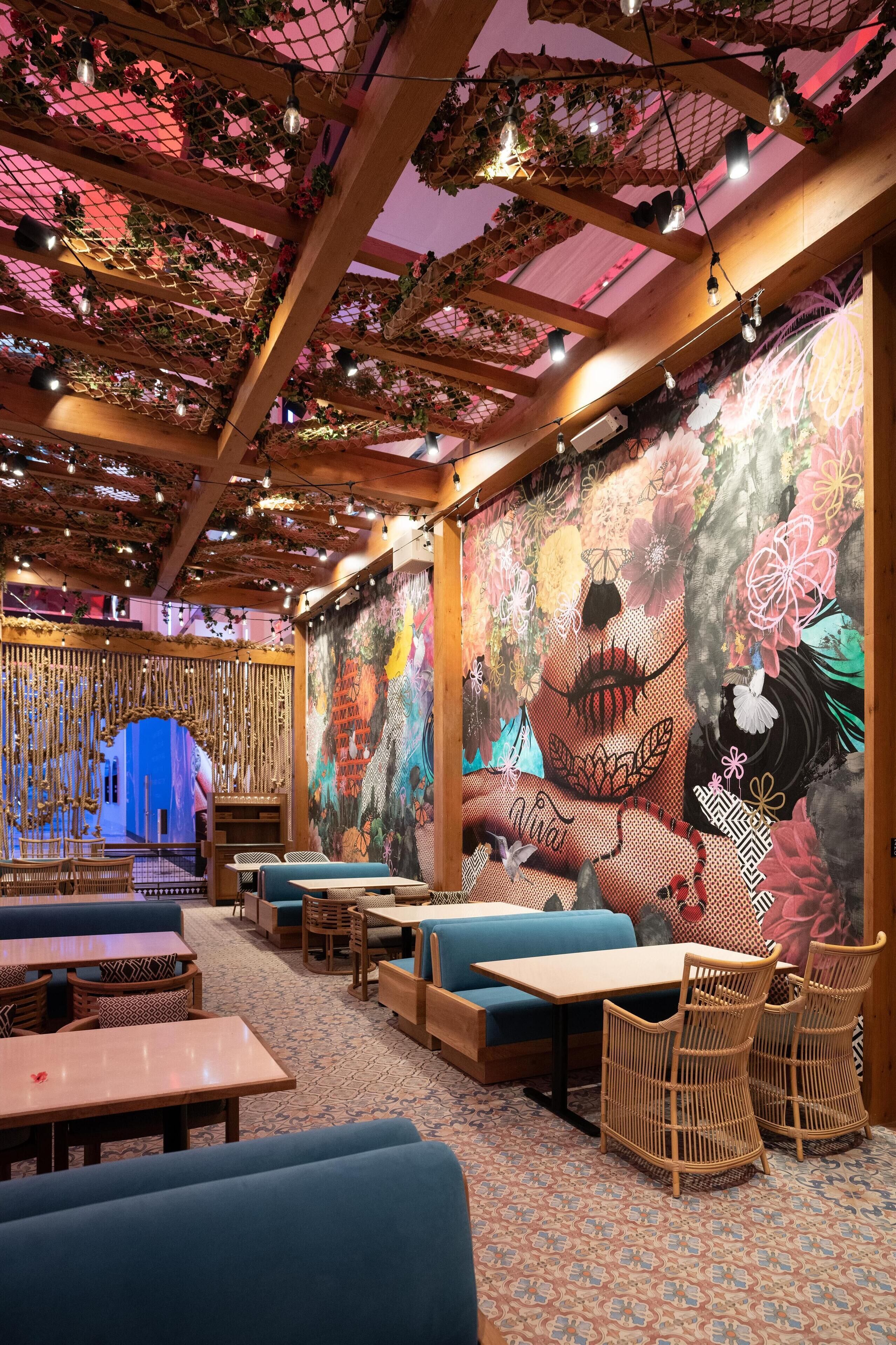 Un restaurante con vigas de madera, plantas colgantes y un mural colorido en la pared.