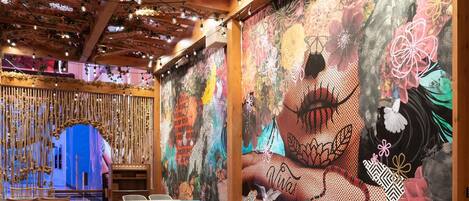 A restaurant with wooden beams, hanging plants, and a colorful mural on the wall.