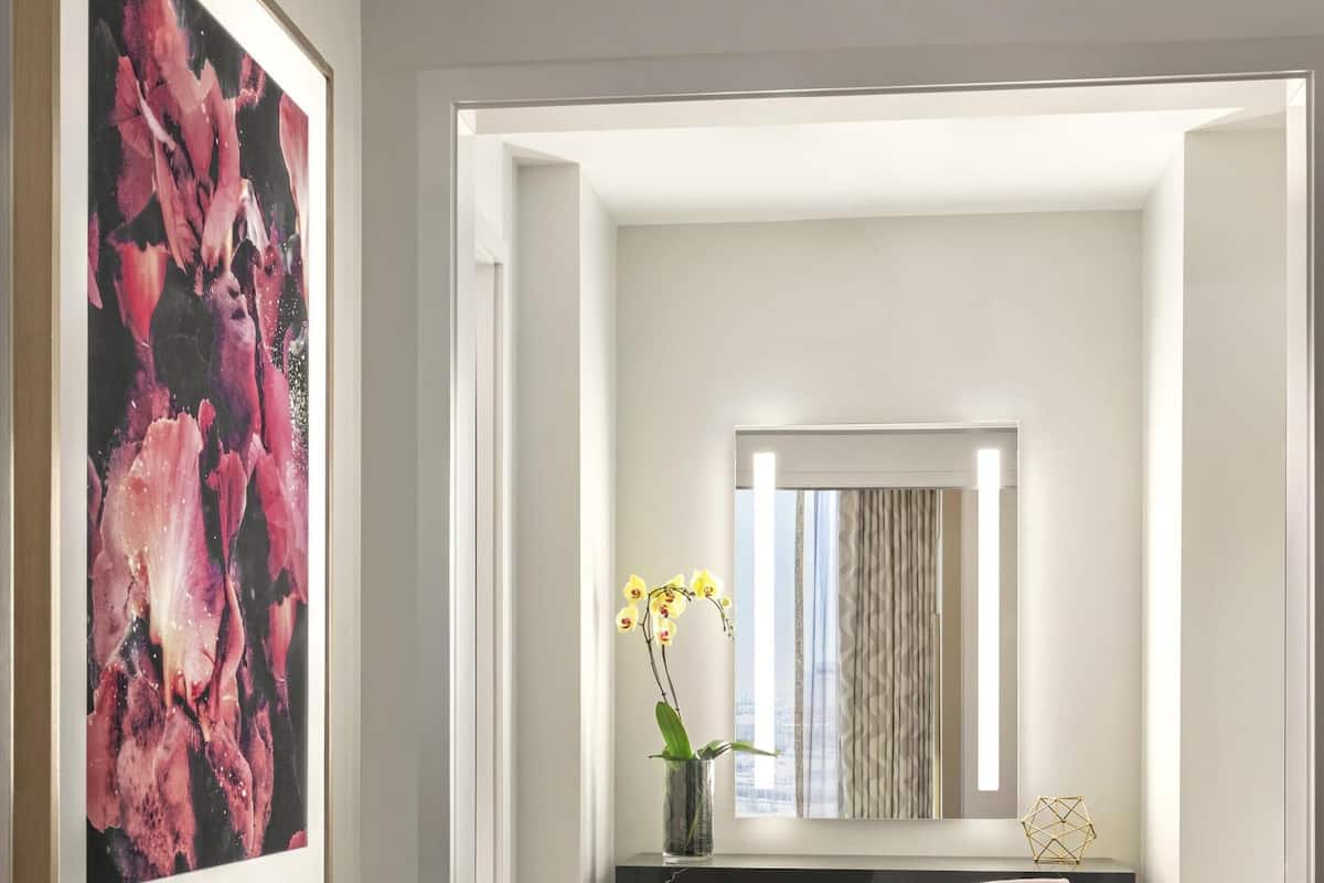 A hallway with a framed abstract painting, a desk with a vase of yellow flowers, and a chair.