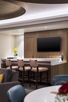 A modern kitchen with a flat-screen TV, bar stools, and a built-in island.