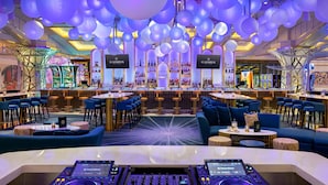 A bar area with multiple seating options, including bar stools and sofas, and a DJ booth in the foreground.