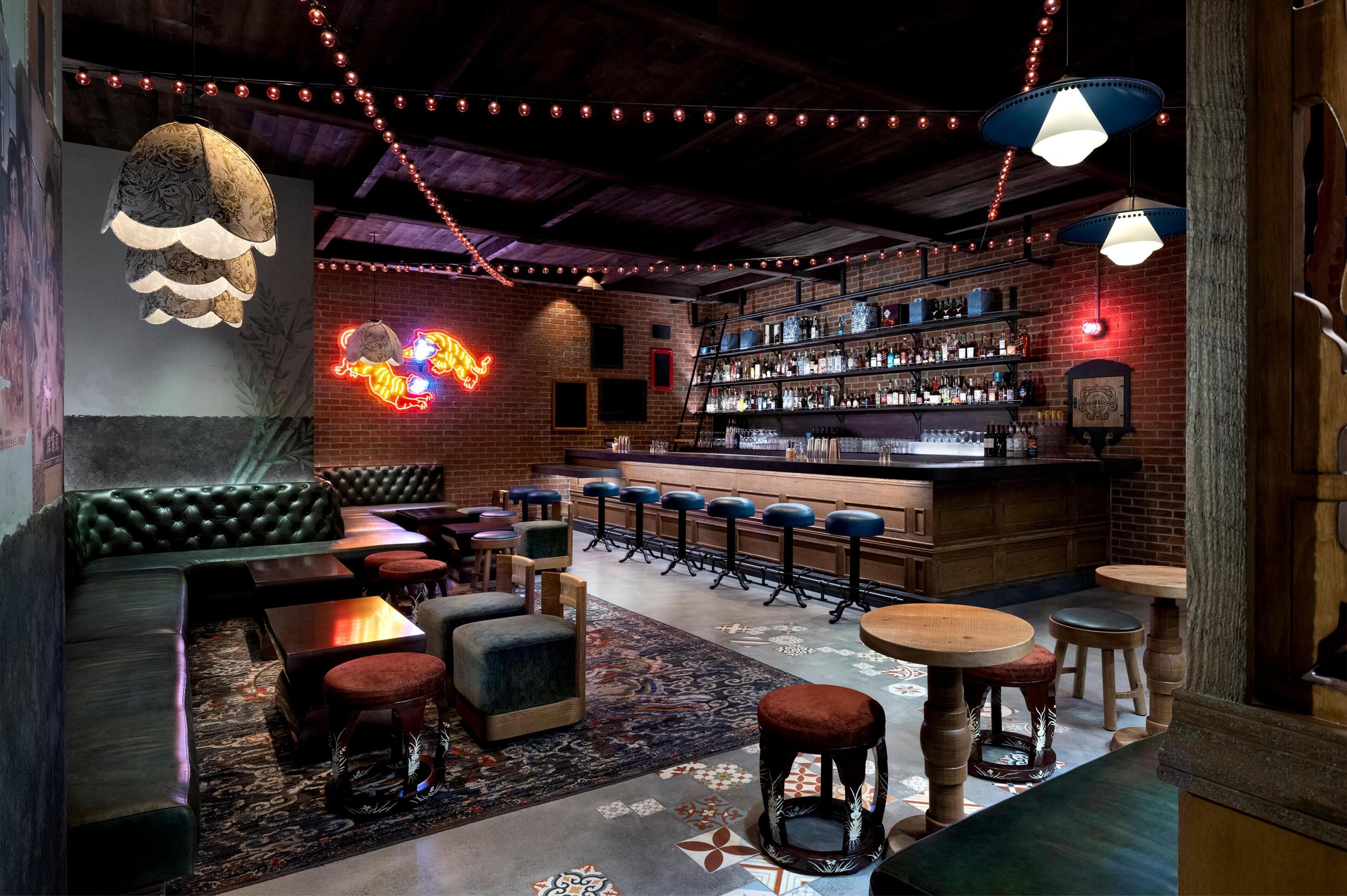 Eine Bar mit Backsteinwand, Holzboden, hängenden Lampen, Barhocker und einem Neonzeichen.