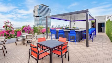 An outdoor patio with a bar area, seating, and a view of a cityscape.