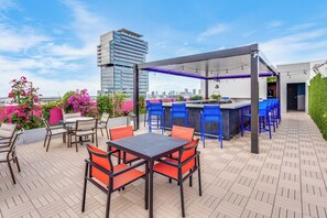 An outdoor patio with a bar area, seating, and a view of a cityscape. - SERENA Hotel Aventura Miami, Tapestry Collection by Hilton (Aventura)