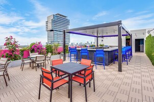 Un patio exterior con área de bar, asientos y vistas de la ciudad.