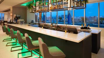 A modern bar area with a long counter, multiple seating options, and a city view.