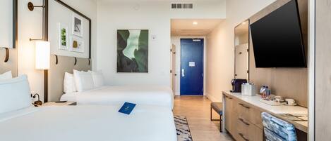 A hotel room with two beds, a flat-screen TV, a desk with a coffee machine, and a large window.