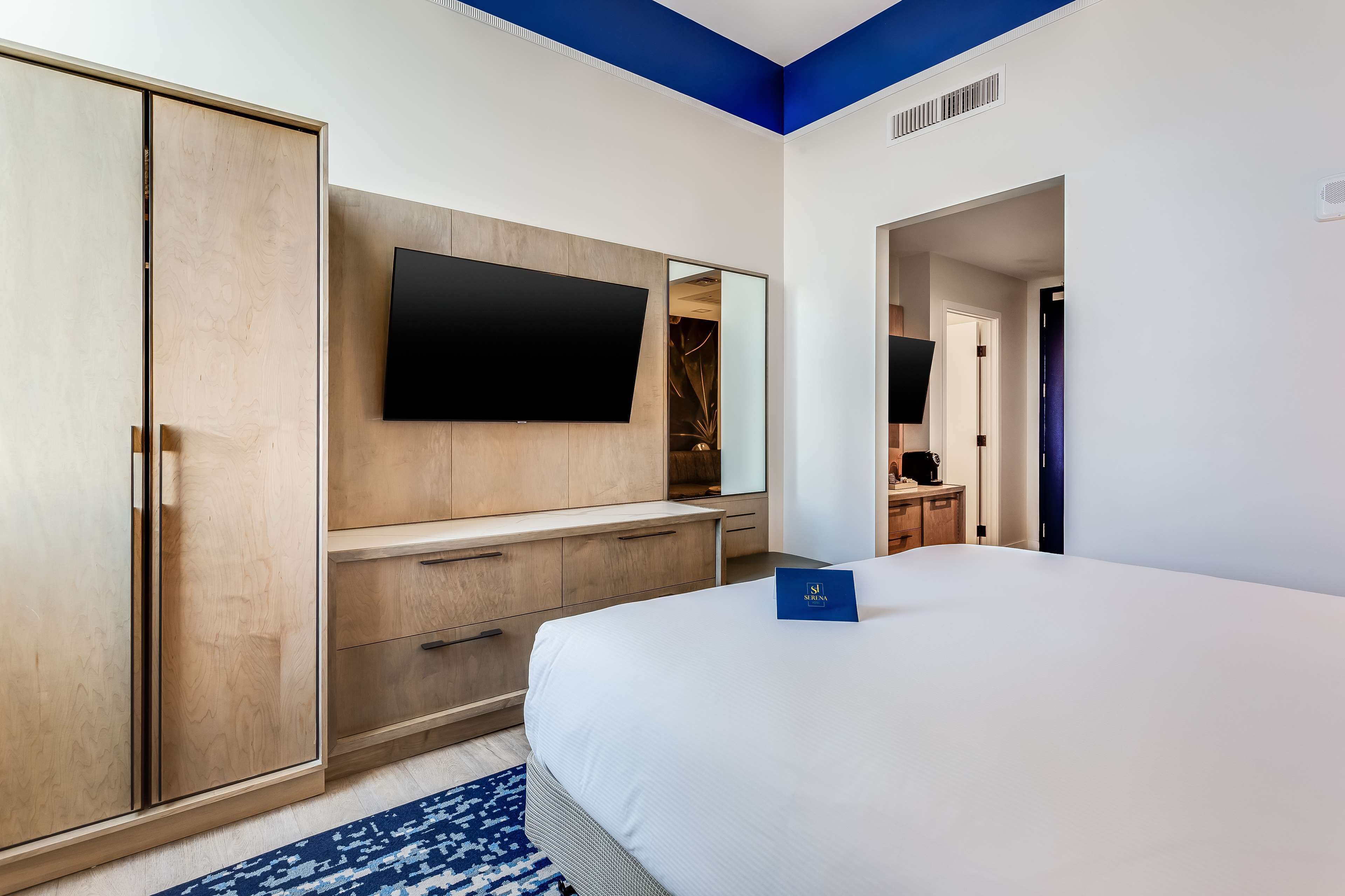 Une chambre d’hôtel comprenant un lit, un téléviseur fixé au mur, une armoire et un bureau avec une chaise.