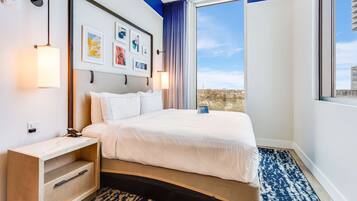Una habitación de hotel con cama, mesita de noche, una obra de arte colgada en la pared y un ventanal con vistas.