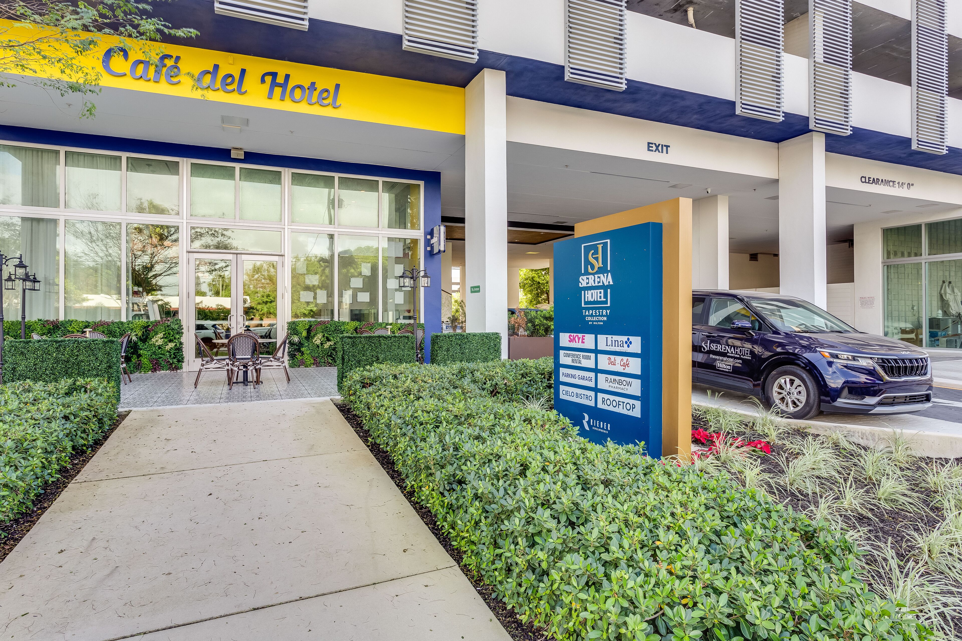A hotel entrance with a 'Cafe del Hotel' sign, a parking garage sign, and a 'Serena Hotel' sign.