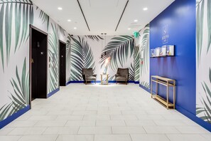 A hotel lobby with a modern design, featuring a herringbone floor pattern, two armchairs, a small table, and a blue accent wall with palm leaf wallpaper. - SERENA Hotel Aventura Miami, Tapestry Collection by Hilton (Aventura)