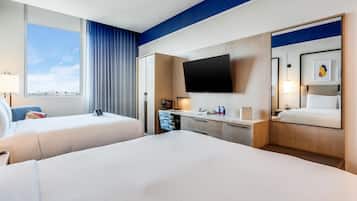 A hotel room with two beds, a flat-screen TV, a desk with a lamp, and a window with curtains.