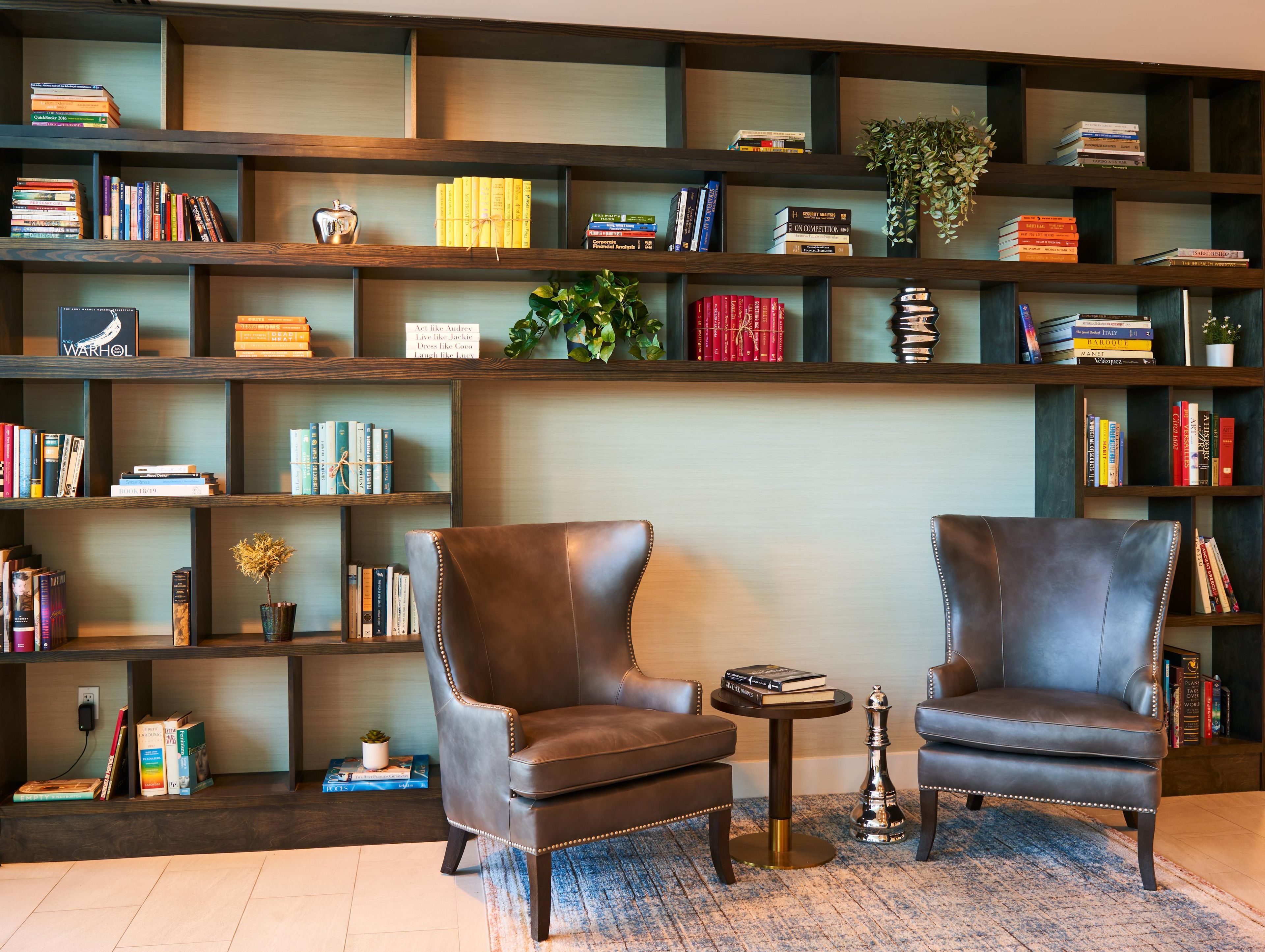 A room with two leather armchairs, a small round table, and a bookshelf filled with books and decorative items.