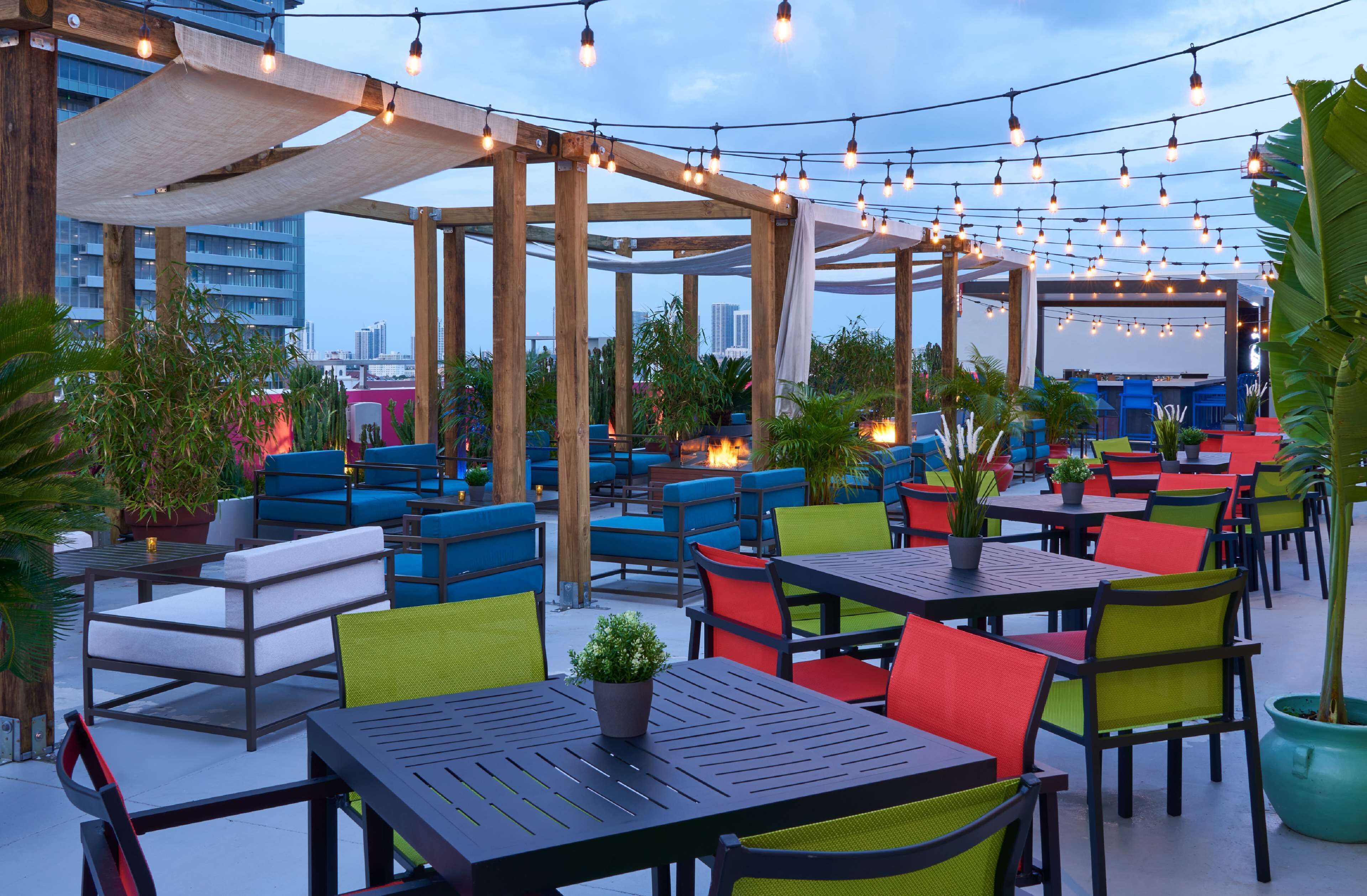 An outdoor seating area with tables and chairs, string lights, and potted plants.