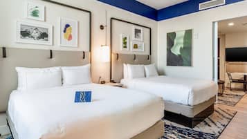 A hotel room with two beds, a desk, a chair, and artwork on the walls.