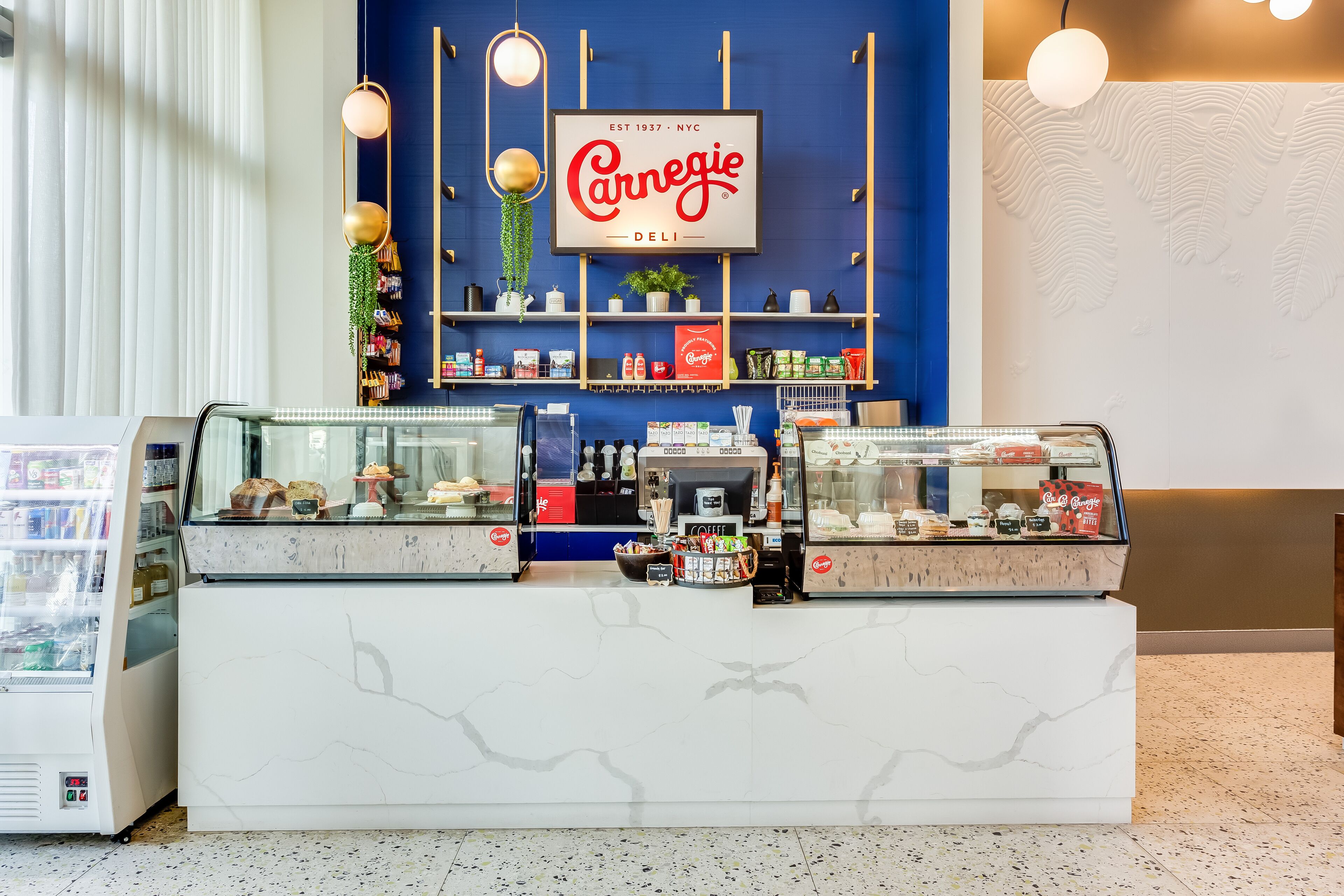 A deli counter with a sign reading "Carnegie Deli," a refrigerated display case, and a coffee machine.