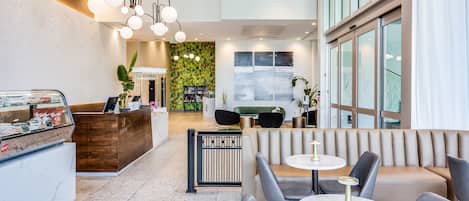 Un moderno vestíbulo con mostrador de recepción, zona de estar y una pared verde con plantas.