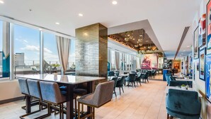 A modern restaurant with a high ceiling, large windows, and a mix of bar and dining areas. - SERENA Hotel Aventura Miami, Tapestry Collection by Hilton (Aventura)