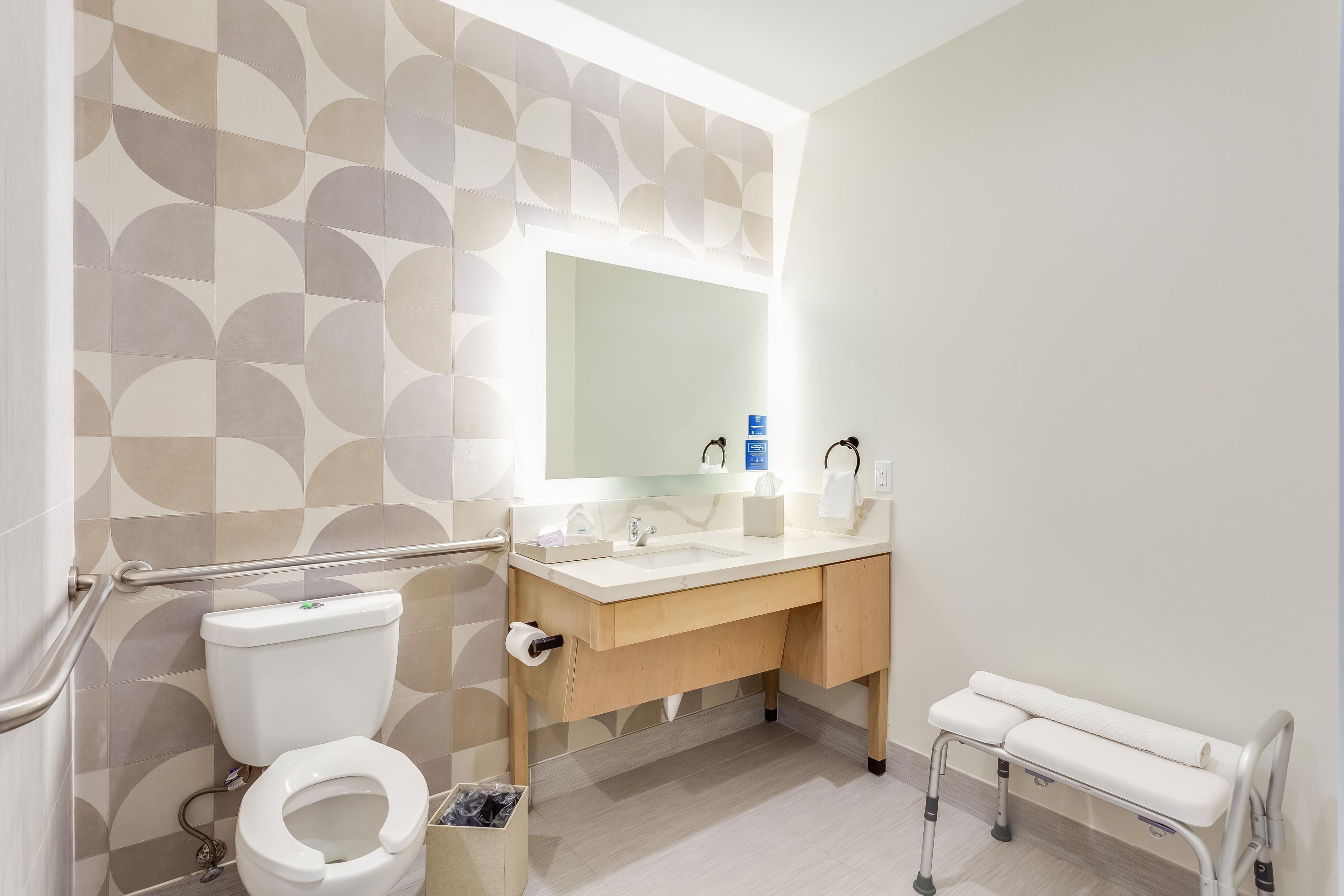 A modern bathroom with a toilet, sink, mirror, and a bench.