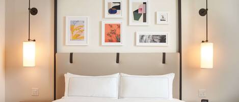 A hotel room with a bed, white bedding, a headboard with artwork, and bedside lamps.