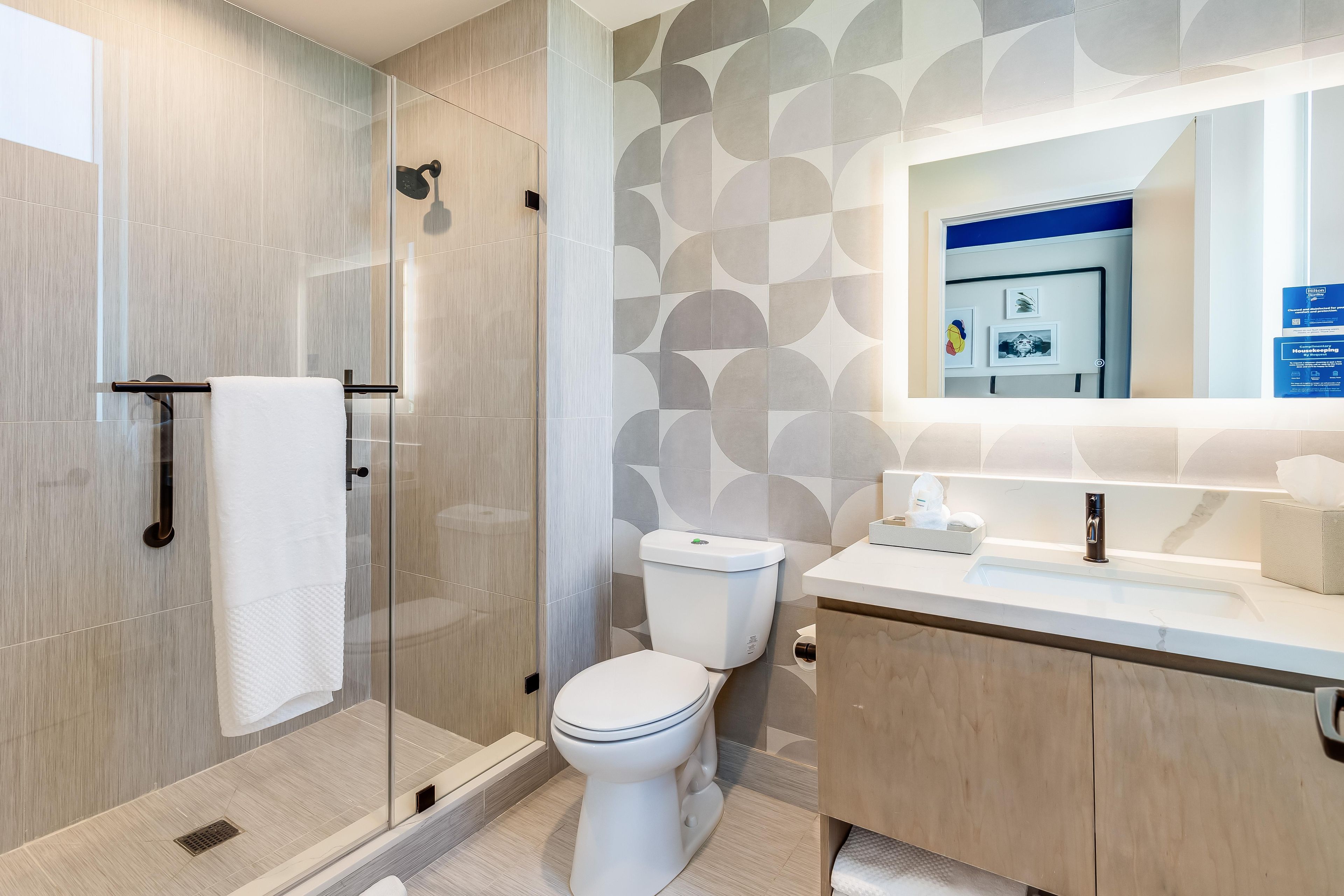 Un bany modern amb dutxa trencada per vidre, un vàter i un lavabo amb mirall.