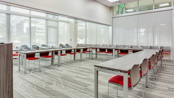 A conference room with long tables and red chairs, large windows, and a carpeted floor.