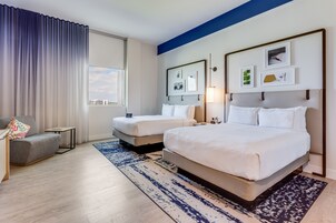 Habitación de hotel con una cama grande, una cama más pequeña, un sofá, una mesita de noche y una ventana con cortinas.