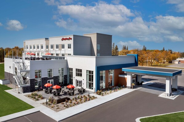 A Hampton Inn hotel with a modern design, outdoor seating area, and a gas station.