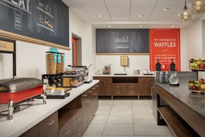 A modern kitchen with a buffet setup, including a red warming tray, food containers, and a large red waffle sign.
