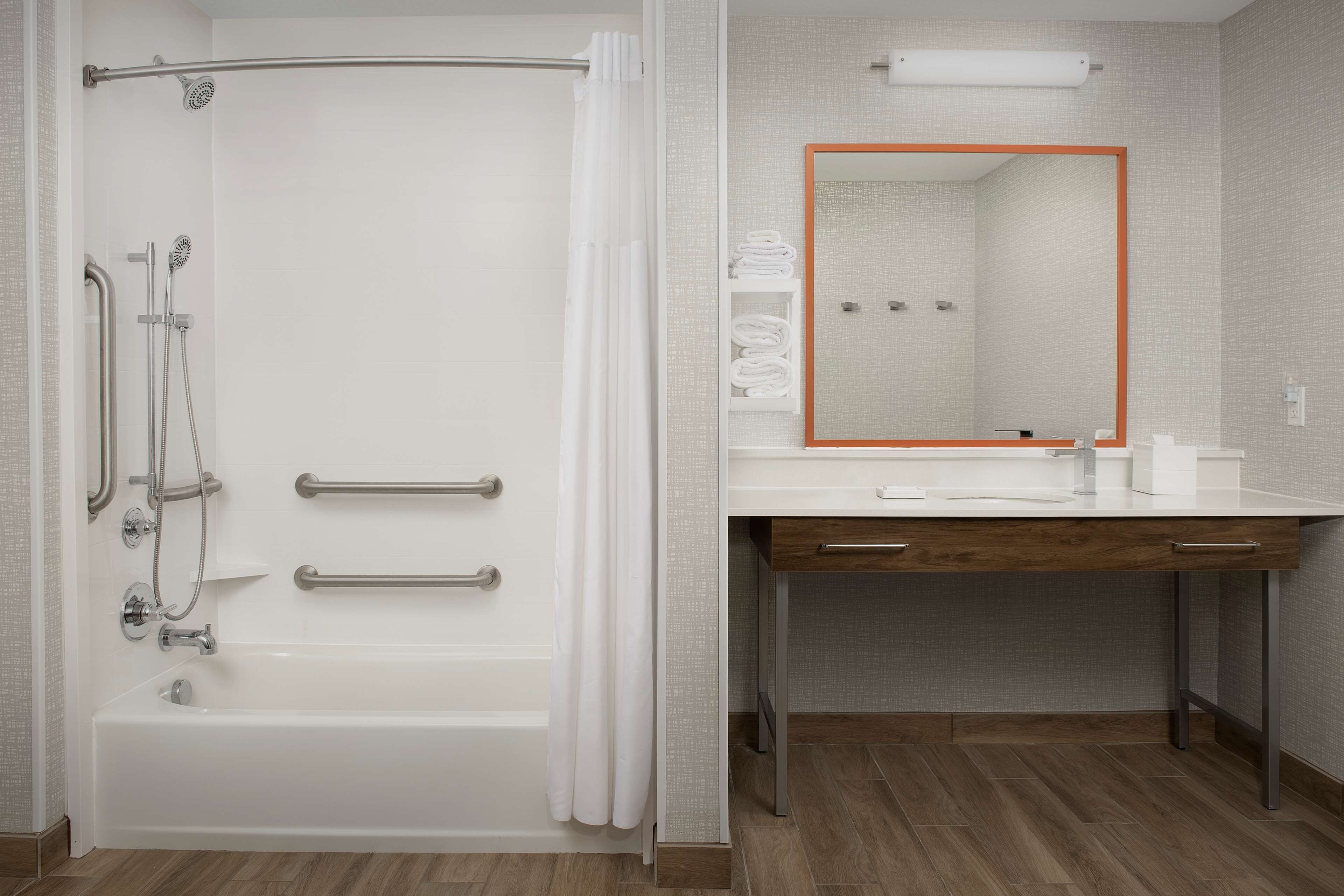 A bathroom with a shower, grab bars, a sink, and a mirror with an orange frame.