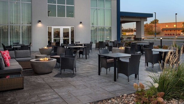 An outdoor patio with seating and fire pits, large windows, and a view of a gas station in the background.