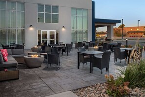 An outdoor patio with seating and fire pits, large windows, and a view of a gas station in the background. - Hampton Inn Warroad, MN (Warroad)