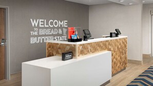 A reception desk with a "WELCOME TO THE BREAD & BUTTER STATE" sign, a water bottle, a bag of chips, and a Hilton Honors card.